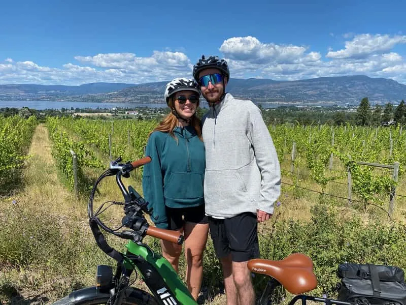 Couple on e-bikes checking a smartphone navigation app at a vineyard gate on the Kelowna self-guided e-bike wine tour along the Okanagan wine trail