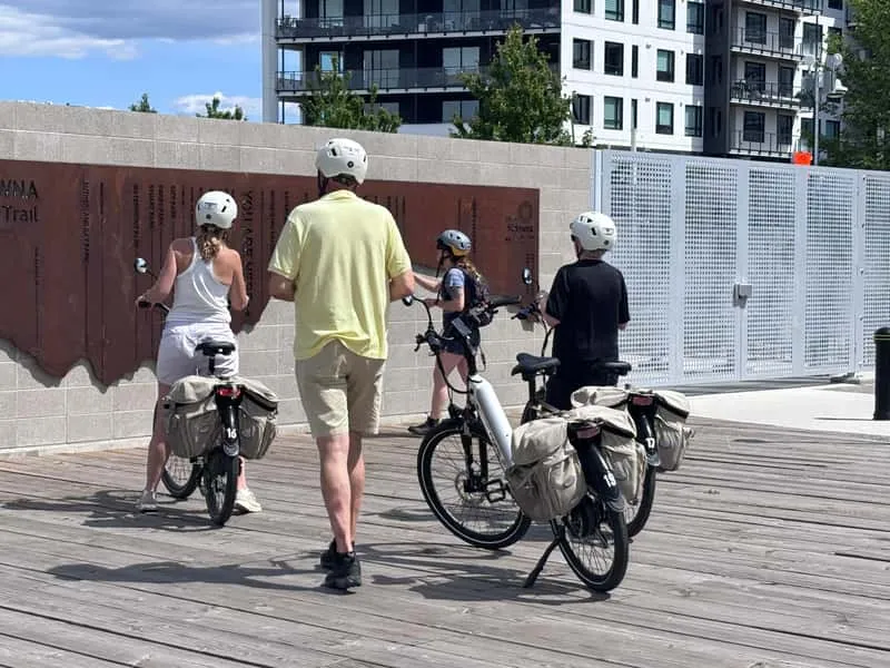 Cyclist checking smartphone navigation on an e-bike near the Okanagan Lake waterfront in Kelowna on a self-guided wine trail tour